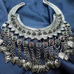 Può includere: Una collana in argento a forma di mezzaluna con punte, pietre rosse e verdi e ciondoli a forma di cuore pendenti.