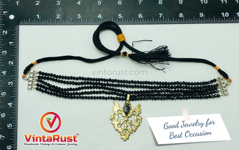 May include: Black beaded choker necklace with a gold-toned pendant. The necklace features multiple strands of small, round beads and a decorative pendant with a black stone. The text "Good Jewelry for Best Occasion" is visible.