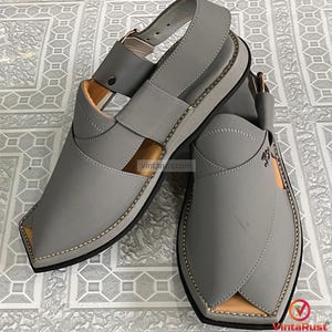 K&ouml;nnte beinhalten: Ein Paar graue Ledersandalen mit Riemen und Schnallenverschluss. Die Sandalen haben ein gen&auml;htes Design an den Kanten und eine hellbraune Innenseite. Die Sohlen sind schwarz, und die Sandalen werden auf einer gemusterten Oberfl&auml;che pr&auml;sentiert.