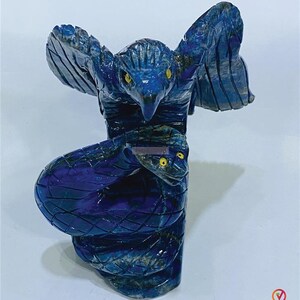 May include: A carved sculpture of a bird with outstretched wings atop a coiled snake. The sculpture is a deep blue color with yellow eyes. The bird's wings are detailed with carved feathers. The snake's scales are also carved.