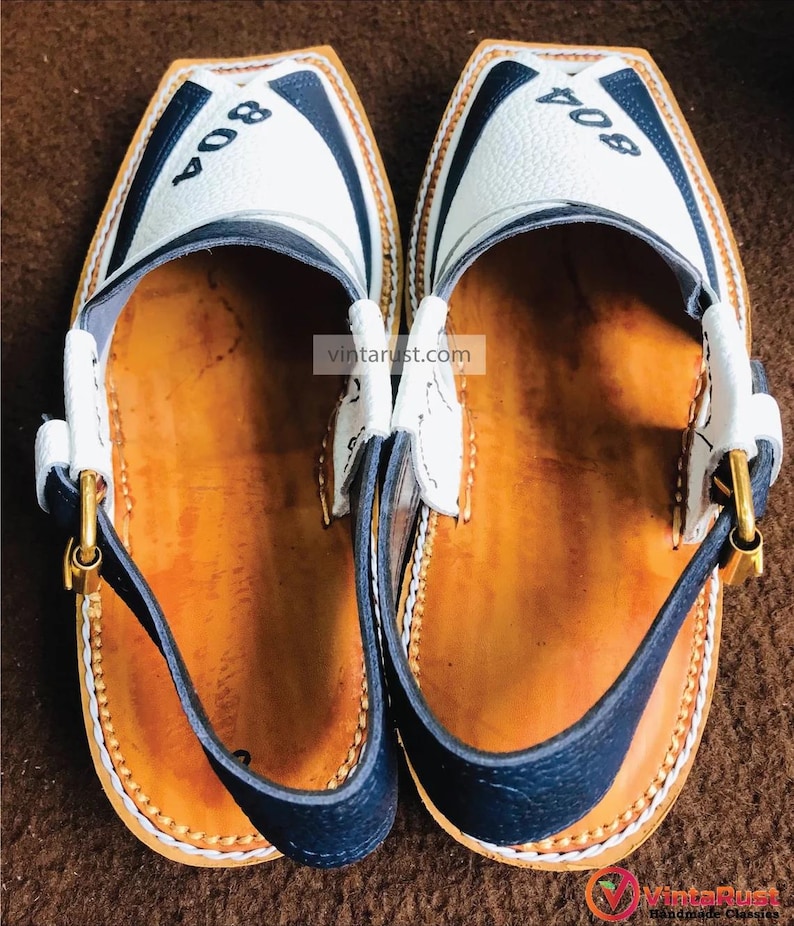 Pu&ograve; includere: Un paio di scarpe in pelle bianca con finiture nere e una fibbia dorata. Le scarpe hanno il numero "804" scritto su di esse.