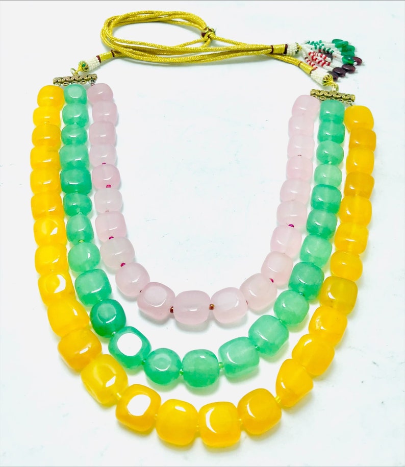 May include: A three-strand necklace with yellow, green, and pink square beads. The necklace has a gold clasp and a yellow cord.