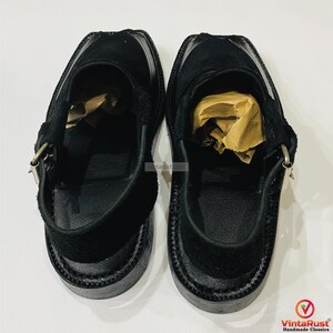 May include: A pair of black leather Peshawari sandals. These open-toe shoes feature a suede upper, a strap with a buckle closure, and a thick sole. The sandals are designed with a traditional silhouette and are suitable for casual wear.