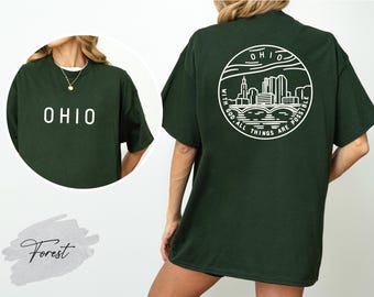 May include: Forest green t-shirt with the word "OHIO" in white block letters on the front. The back of the shirt features a white circular design with the word "OHIO" and a skyline graphic, with the text "WITH GOD ALL THINGS ARE POSSIBLE".
