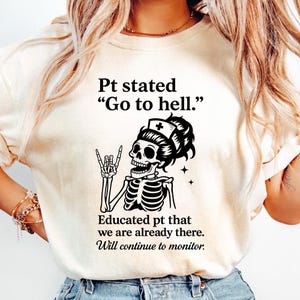 May include: Cream-colored t-shirt with a black graphic of a skeleton nurse giving a rock-and-roll hand gesture. Text reads "Pt stated 'Go to hell.' Educated pt that we are already there. Will continue to monitor."