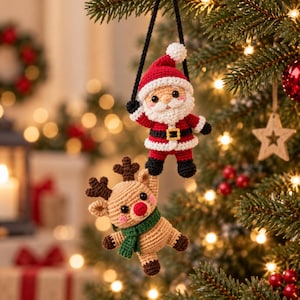 Könnte beinhalten: Ein gehäkelter Weihnachtsmann-Anhänger in rot-weißem Anzug mit schwarzem Gürtel und ein gehäkelter Rentier-Anhänger in Beige mit grünem Schal, beide an einer schwarzen Schnur vor einem unscharfen, geschmückten Weihnachtsbaum hängend.
