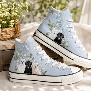 May include: A pair of light blue high-top sneakers featuring detailed embroidery of dogs and white flowers. The shoes have white laces, white rubber toe caps, and white soles with black trim lines. The embroidery depicts three dogs on one shoe.