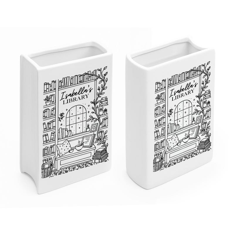Puede incluir: Dos jarrones blancos de cer&aacute;mica con forma de libro. Cada jarr&oacute;n presenta una ilustraci&oacute;n en blanco y negro de una escena de biblioteca con el texto "Isabella's Library". El dise&ntilde;o incluye estanter&iacute;as, una ventana y un rinc&oacute;n de lectura.