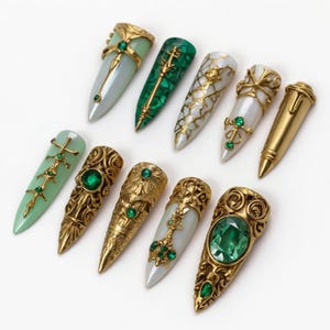 May include: An assortment of ten ornate, pointed nail designs. The nails feature gold and jewel embellishments, including emerald green and pearl-like accents. Some nails have a malachite green or pale green base, while others are white or gold.