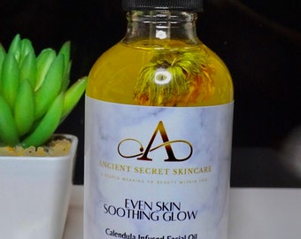 May include: A clear glass bottle of Calendula Infused Facial Oil with a black dropper. The bottle contains yellow liquid and flower petals. The label reads "Ancient Secret Skincare" and "Even Skin Soothing Glow". The bottle contains 4 fl oz.