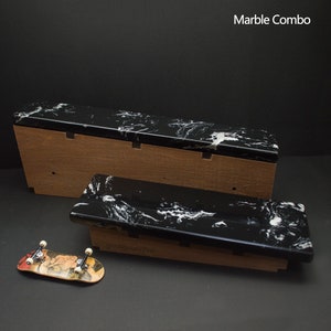 May include: A black and white marble-patterned fingerboard ramp set with a wooden base. The set includes two ramps and a miniature skateboard with a colorful design. The text "Marble Combo" is visible.