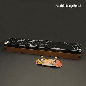 Peut inclure: Un long banc en marbre noir et blanc avec une base en bois. Un petit skateboard avec un motif floral est devant le banc. Le texte "Marble Long Bench" est visible. Le banc mesure environ 30 cm de long.