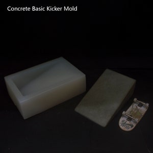 Könnte beinhalten: Eine weiße rechteckige Form und eine graue Betonrampe für ein Miniatur-Skateboard. Der Text "Concrete Basic Kicker Mold" steht oben. Ein kleines Skateboard befindet sich neben der Rampe.