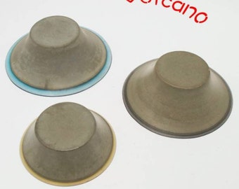 May include: Three gray, volcano-shaped objects with a circular base. One has a blue rim, another a yellow rim, and the third has a gray rim. The word "Volcano" is written in red above the objects.