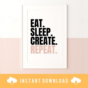May include: A white framed print with black text that reads "Eat. Sleep. Create. Repeat." The print is on a white wall with a light pink wall below it.