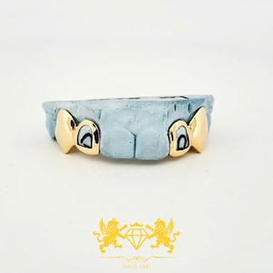 Puede incluir: Grill de oro con dos dientes en forma de corazón, colocado en un molde azul.