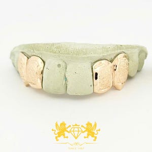 Puede incluir: Grill de dientes de oro con acabado texturizado, mostrado en un molde de boca.