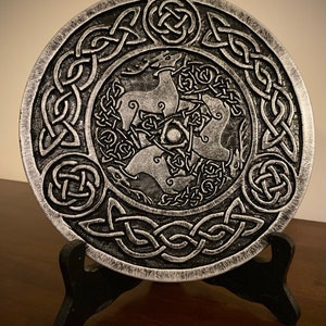 May include: A silver metal plate with a Celtic knot design and three stylized deer in the center. The plate is on a black stand.