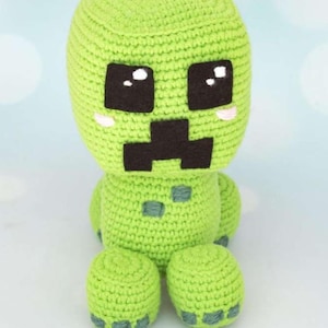Pode incluir: Um brinquedo de pelúcia Creeper verde de crochê feito à mão. O brinquedo apresenta uma cabeça quadrada com olhos e boca pretos e um corpo verde claro. A pelúcia está sentada com as pernas estendidas. O brinquedo é um personagem popular do videogame Minecraft.
