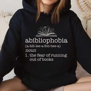 May include: A black hoodie with a white graphic design that reads "abibliophobia (a-bib-lee-a-foh-bee-a) noun 1. the fear of running out of books".