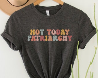 May include: A dark grey t-shirt with the text "NOT TODAY PATRIARCHY" printed in rainbow colors.