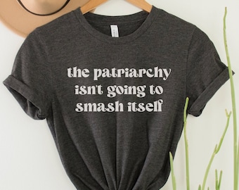 May include: A dark grey t-shirt with the text "the patriarchy isn't going to smash itself" printed in white.