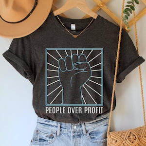 May include: A dark gray t-shirt with a raised fist graphic and the text "People Over Profit" in white lettering.