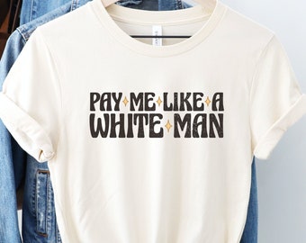 Puede incluir: Una camiseta blanca con el texto "PAY ME LIKE A WHITE MAN" en negro con estrellas doradas.