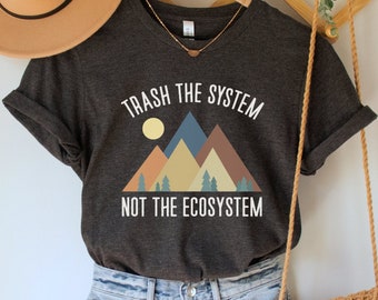 May include: A dark gray t-shirt with a white graphic of mountains and a sun. The text on the shirt reads "Trash the system, not the ecosystem".