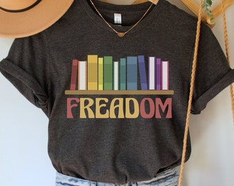 May include: A dark grey t-shirt with a rainbow bookshelf graphic and the text "FREEDOM" in a retro font.