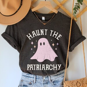 May include: A dark gray t-shirt with a pink ghost graphic and the text "Haunt the Patriarchy".