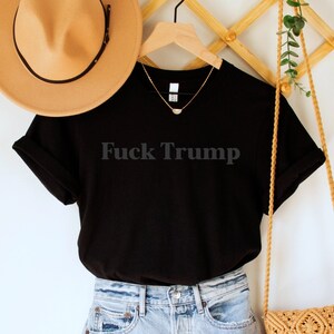 A black unisex crew neck short sleeve Bella Canvas t-shirt that says "Fuck Trump" in dark grey, tone-on-tone lettering