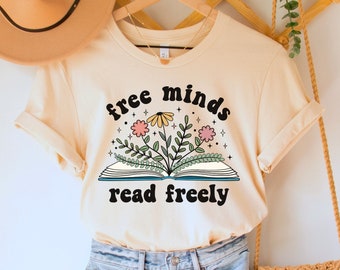 May include: A light beige t-shirt with the text "free minds read freely" in black. The text is surrounded by a stylized open book with flowers and leaves.
