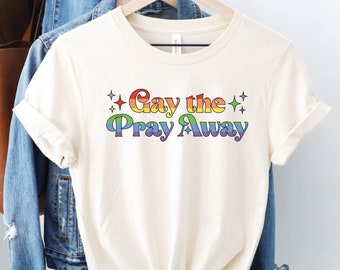 May include: A white t-shirt with the text "Gay the Pray Away" in rainbow colors with stars on either side of the text.