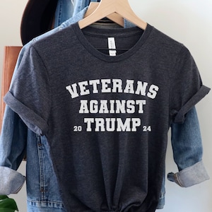 May include: A dark gray t-shirt with the text "Veterans Against Trump 20 24" printed in white.