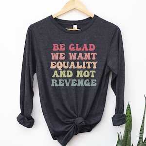 May include: A dark grey long-sleeved t-shirt with the text "BE GLAD WE WANT EQUALITY AND NOT REVENGE" printed in rainbow colors.