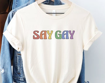 May include: A white t-shirt with the text "SAY GAY" in rainbow colors.