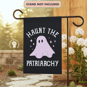 May include: A black garden flag with the text "HAUNT THE PATRIARCHY" and a light purple ghost illustration. The flag is displayed on a black metal stand in a garden setting. The words "STAND NOT INCLUDED" are at the top.