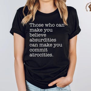 May include: Black t-shirt with the quote "Those who can make you believe absurdities can make you commit atrocities" in white text. The shirt also has a small graphic that says "10% DONATED TO SOCIAL JUSTICE".