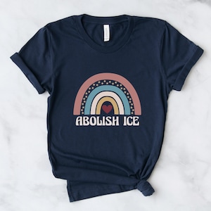 May include: A navy blue t-shirt with a rainbow graphic and the text "ABOLISH ICE" in white. The rainbow is made up of pink, blue, yellow, and orange stripes with a red heart in the center.