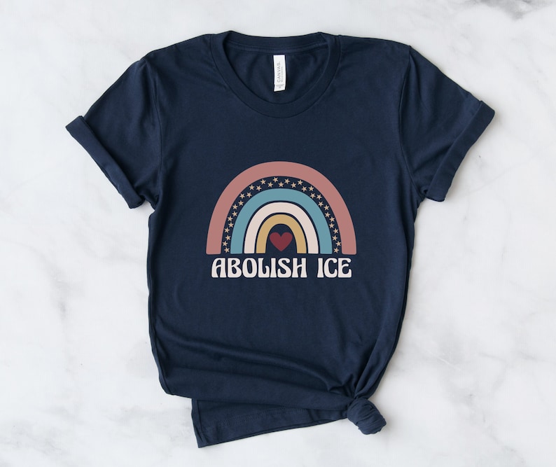 May include: A navy blue t-shirt with a rainbow graphic and the text "ABOLISH ICE" in white. The rainbow is made up of pink, blue, yellow, and orange stripes with a red heart in the center.