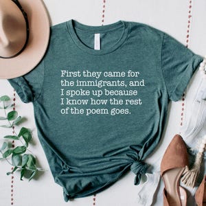 A heather forest green unisex short sleeve crew neck t-shirt that says "First they came for the immigrants, and I spoke up because I know how the rest of the poem goes." in white typewriter font on the chest.
