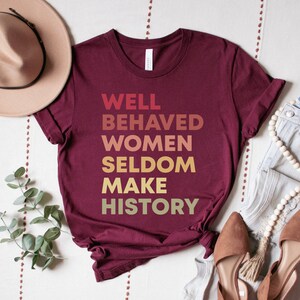 May include: Burgundy t-shirt with the text "WELL BEHAVED WOMEN SELDOM MAKE HISTORY" in a gradient of yellow, orange, and red.