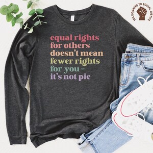 May include: A dark gray long-sleeve shirt with the text "equal rights for others doesn't mean fewer rights for you - it's not pie" printed in rainbow colors.