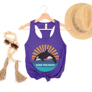 A purple women's racerback tank top that says "sink the rich" in white over a retro graphic of an orca whale in the ocean