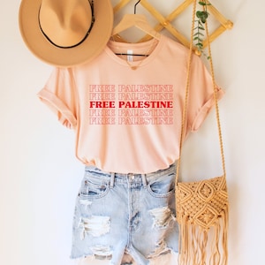A heather peach unisex crew neck t-shirt with red text saying "Free Palestine" 5 times, with the middle text full red and the top and bottom 2 just a red outline