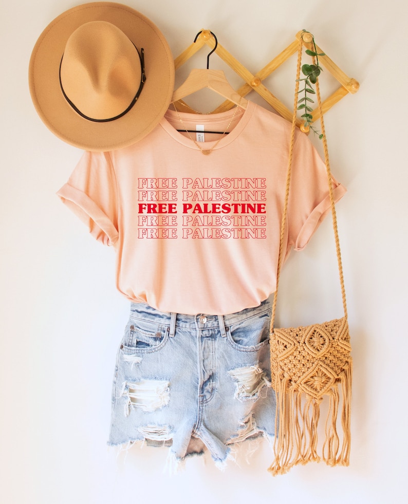 A heather peach unisex crew neck t-shirt with red text saying "Free Palestine" 5 times, with the middle text full red and the top and bottom 2 just a red outline