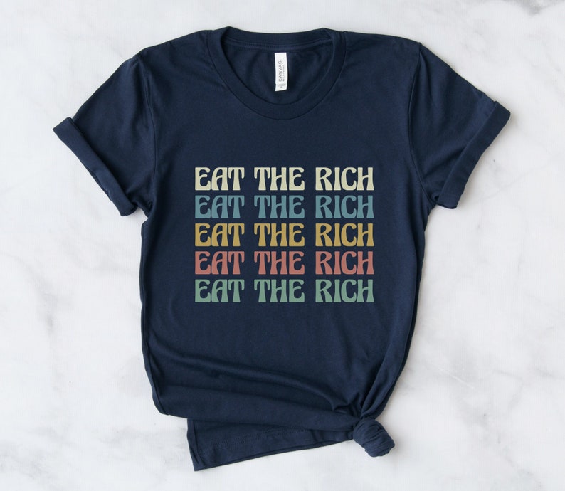 A navy blue unisex crew neck short sleeve Bella Canvas t-shirt that says "eat the rich" repeated 5 times in retro font and colors