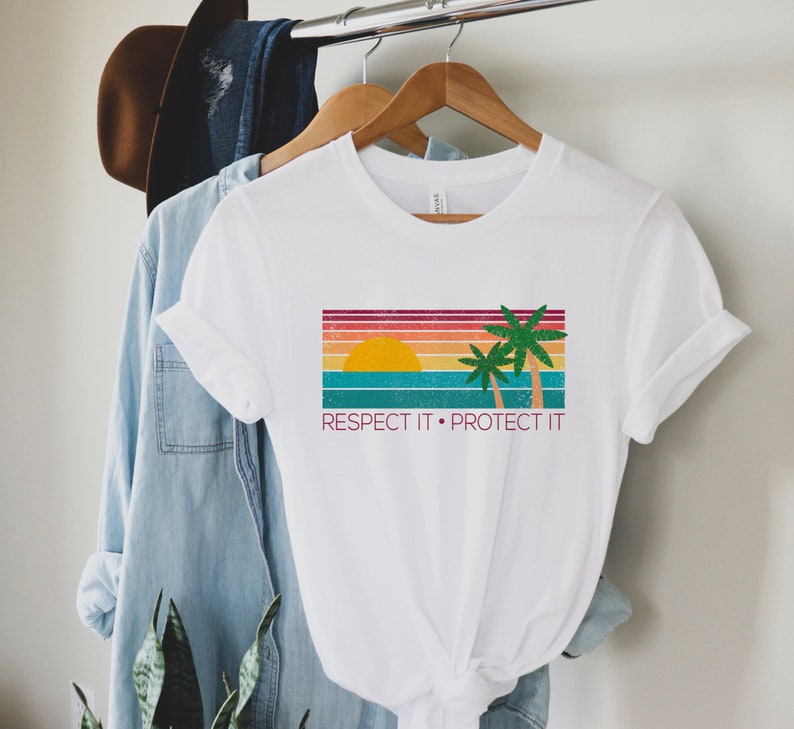 May include: White t-shirt with a retro sunset and palm trees graphic. The text "Respect It. Protect It" is printed below the graphic.