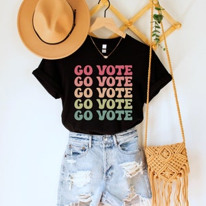 A black unisex crew neck short sleeve t-shirt that says "go vote" repeating 5 times in pastel colors